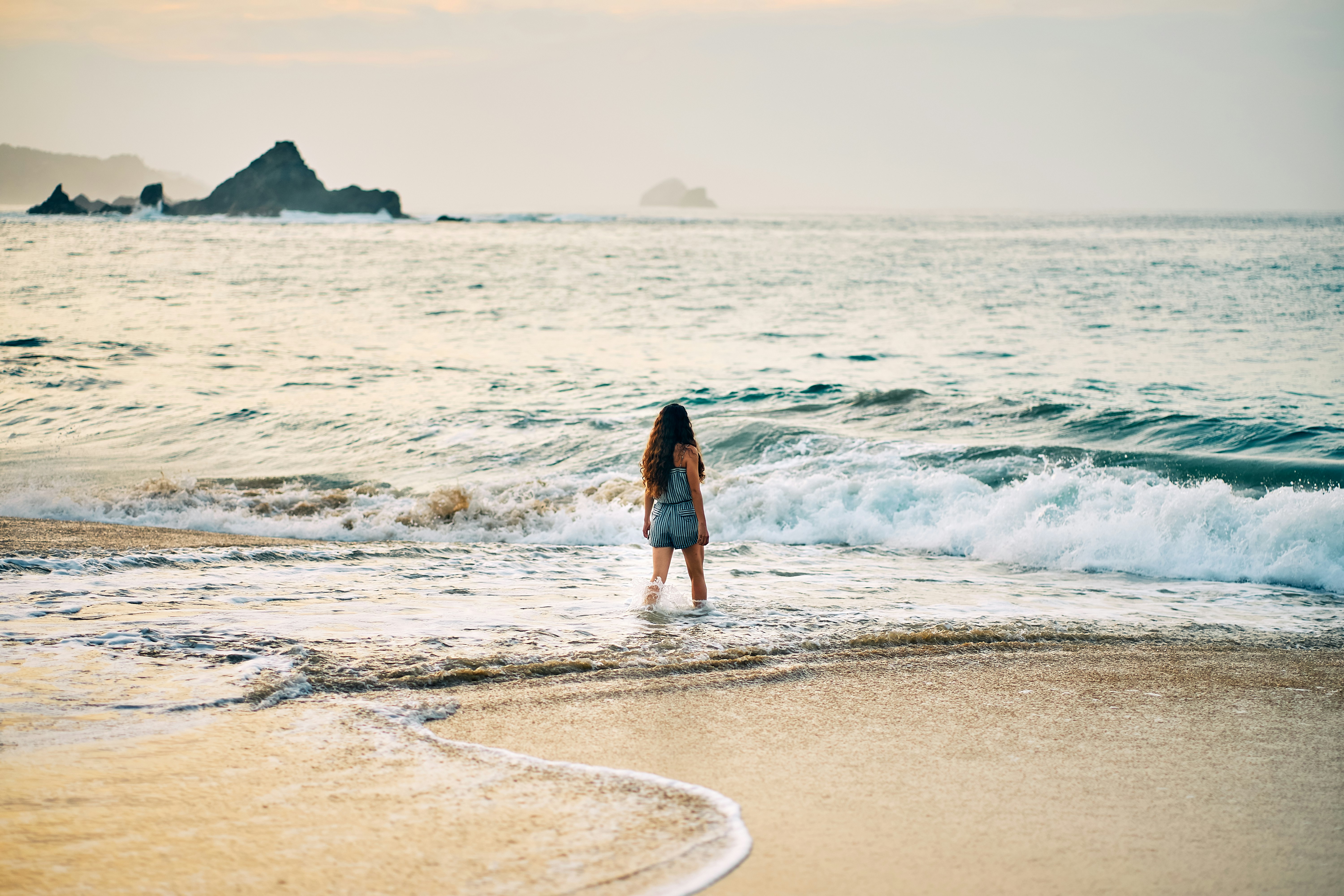 woman in black dress walking on beach during daytime