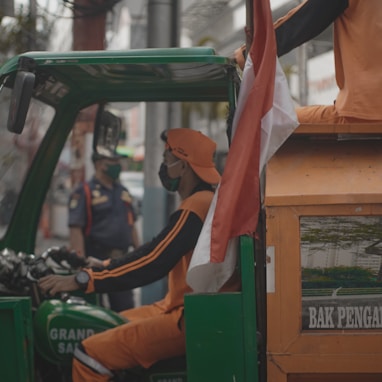 man in orange t-shirt and blue denim jeans sitting on orange and green auto rickshaw