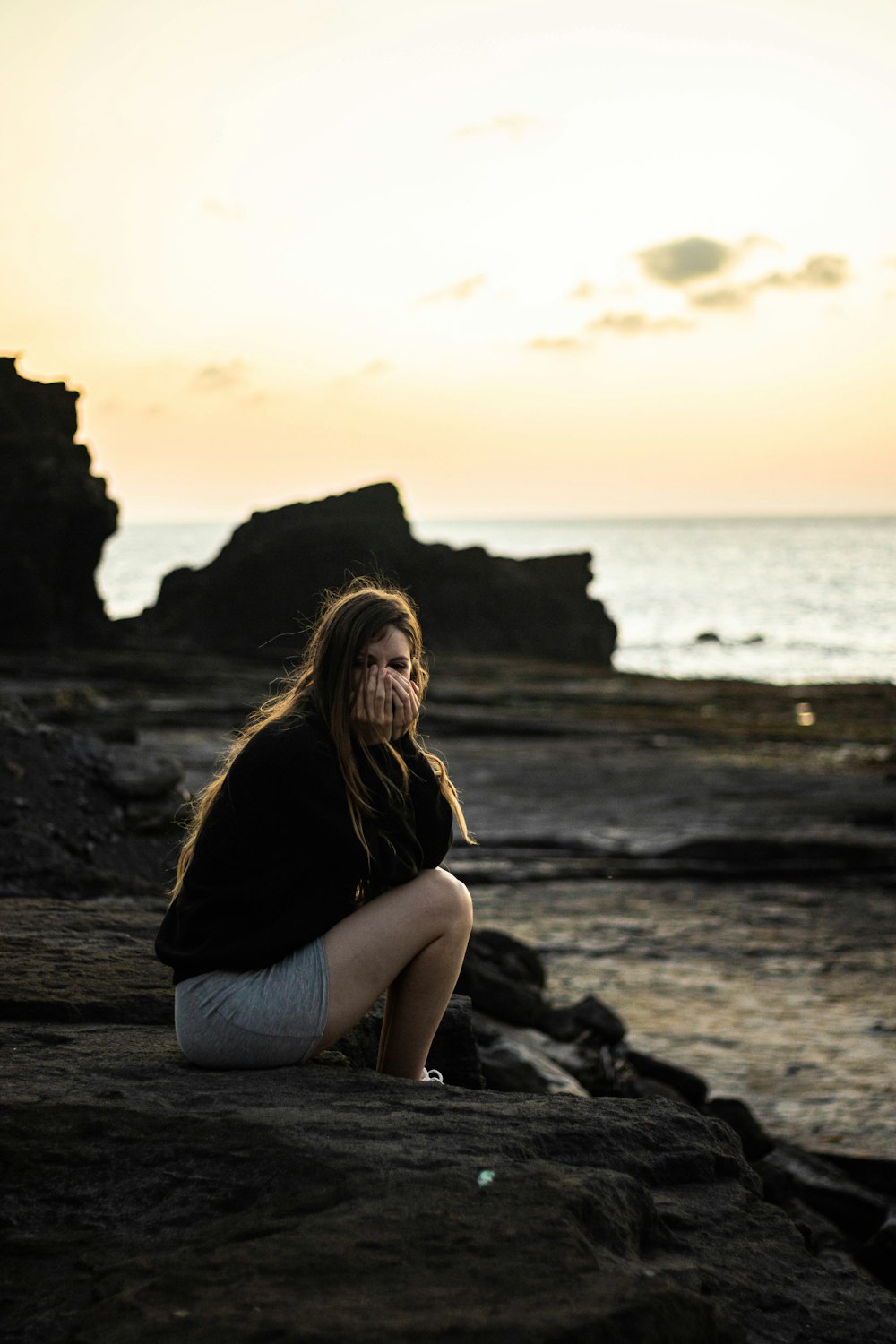 woman in black shirt sitting on rock near sea during daytime