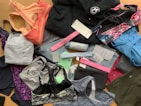 A collection of various athletic apparel and accessories laid out, including sports bras, tops, headbands, and tags. The items are in different colors and patterns, such as pastel pink, blue, and floral designs. A black jacket and several pieces still have brand tags attached.