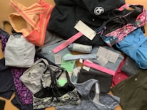 A collection of various athletic apparel and accessories laid out, including sports bras, tops, headbands, and tags. The items are in different colors and patterns, such as pastel pink, blue, and floral designs. A black jacket and several pieces still have brand tags attached.