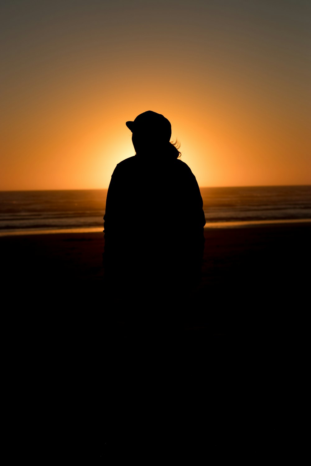 silhouette of person wearing hat standing on beach during sunset