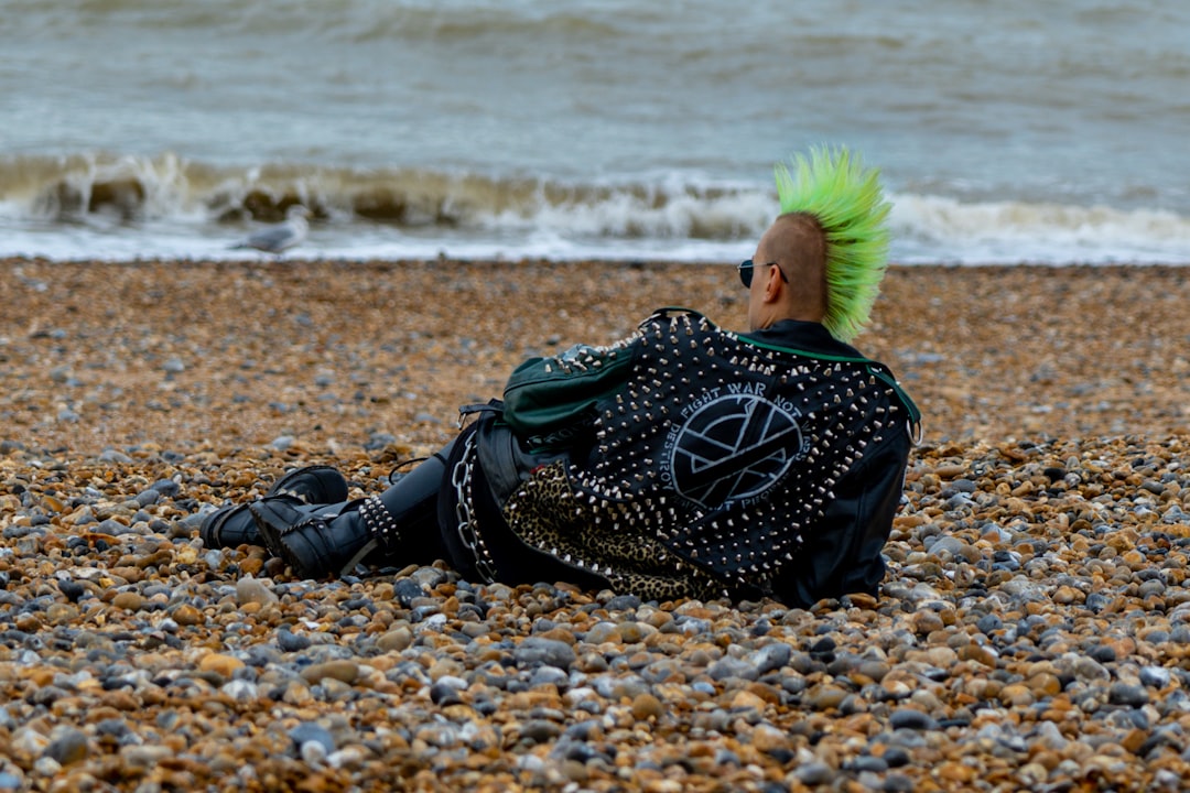 A punk rocker, dressed in leather, with green Mohican hair and wearing sunglasses, laying on the beach.