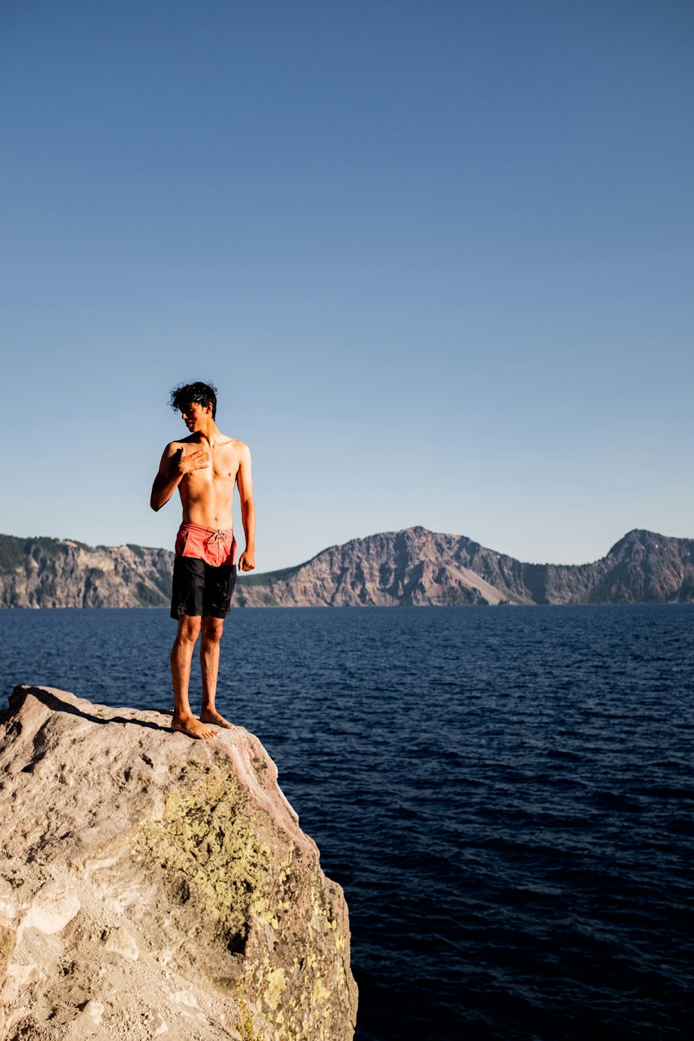 man in black shorts standing on rock formation near body of water during daytime