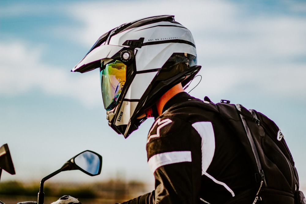 homem em jaqueta preta e branca vestindo capacete preto e óculos pretos