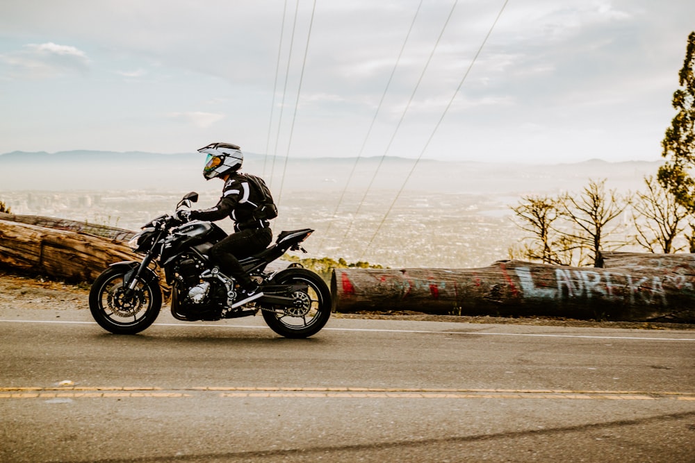 a man riding a motorcycle down a street next to a forest