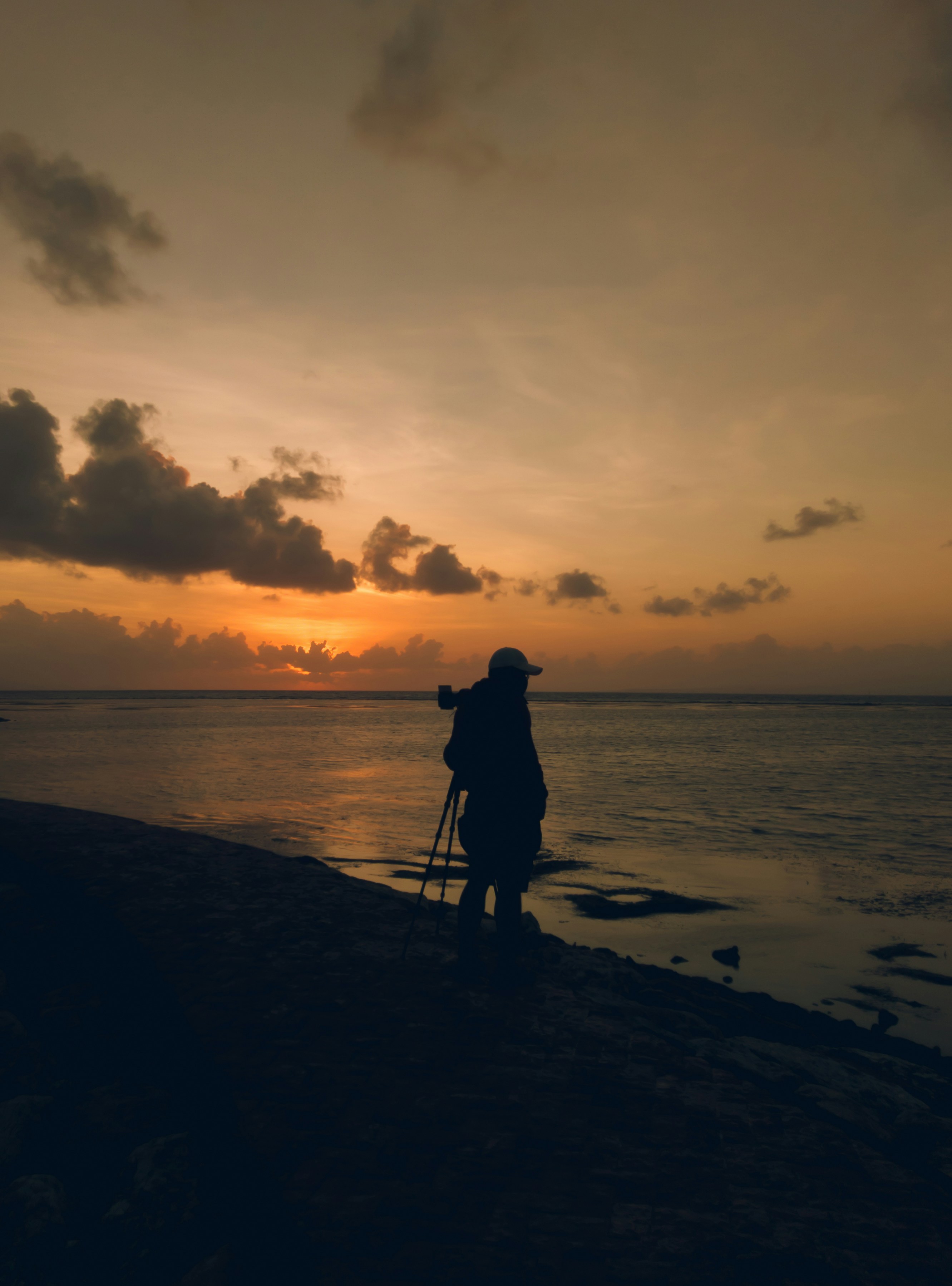 Photographer silhouette at sunset with tripod, dramatic sky, golden hour light