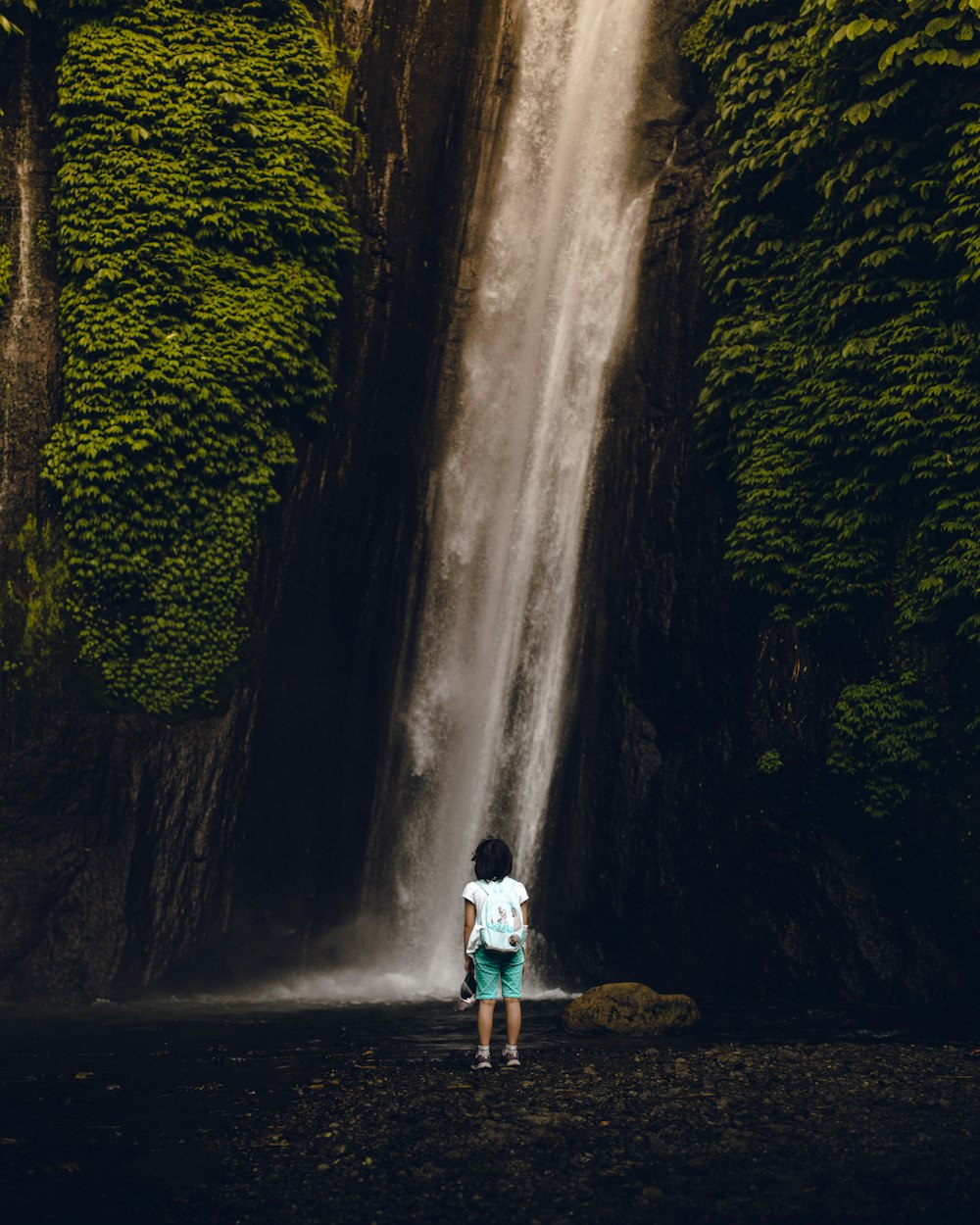 woman in white shirt standing on rock near waterfalls during daytime