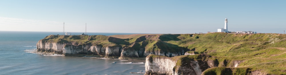 green grass field on cliff by the sea under blue sky during daytime