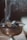 A metal incense burner is seen with smoldering charcoal and a piece of resin releasing smoke. The smoke curls and rises in delicate swirls against a blurred background, suggesting a serene and calm atmosphere.