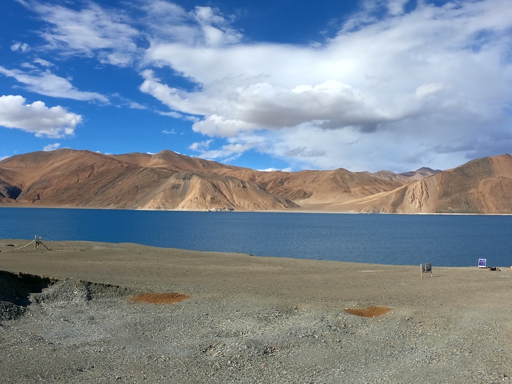 person standing on seashore near mountain under blue sky during daytime