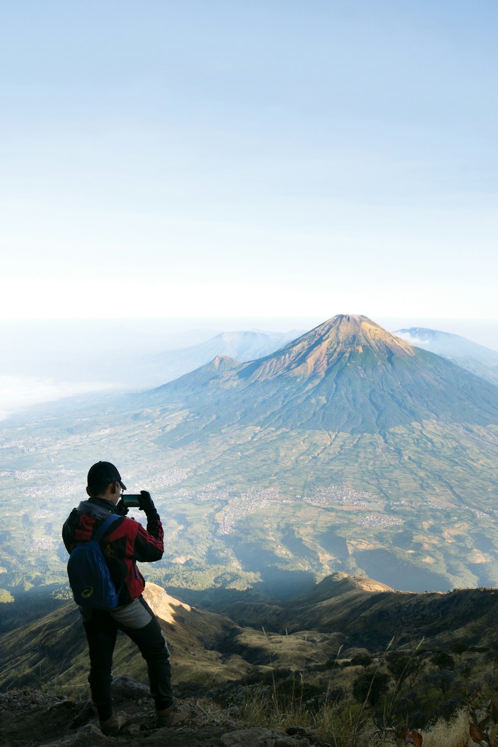 man in blue jacket taking photo of mountain during daytime