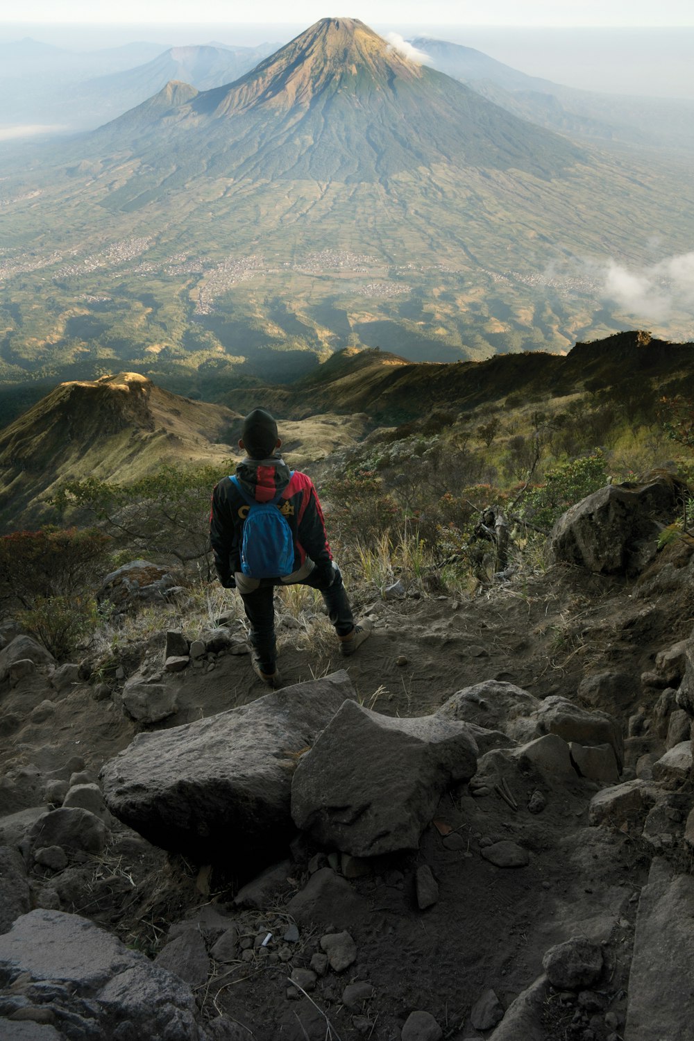 man in blue jacket and black pants standing on rock mountain during daytime