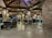 A well-lit restaurant with rustic wooden ceilings and stone pillars. There are multiple tables and chairs, some of which are empty while others are occupied by people dining. The ambiance appears cozy and inviting, with warm lighting fixtures hanging from the ceiling.