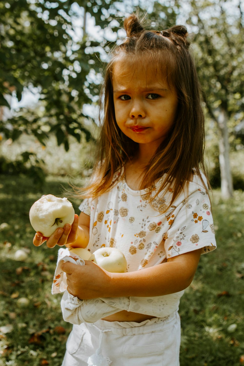 girl in white yellow and pink floral dress holding white apple