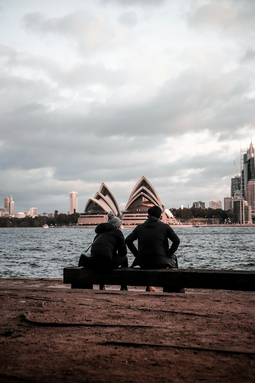 couple sitting on brown wooden bench near body of water during daytime