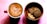 A cup of coffee with intricate latte art sits beside a wooden bowl filled with assorted cookies. The coffee is in a red mug, creating a pleasing contrast with the crema. The arrangement is placed on a pink textured background, enhancing the warm, inviting atmosphere.