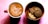 A cup of coffee with intricate latte art sits beside a wooden bowl filled with assorted cookies. The coffee is in a red mug, creating a pleasing contrast with the crema. The arrangement is placed on a pink textured background, enhancing the warm, inviting atmosphere.
