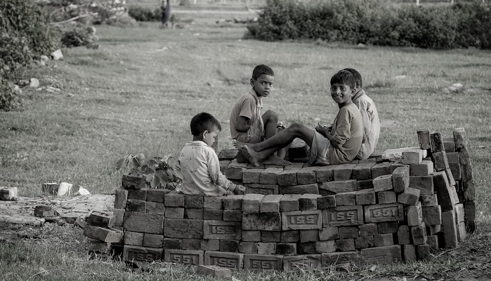 3 boys sitting on brown bricks during daytime