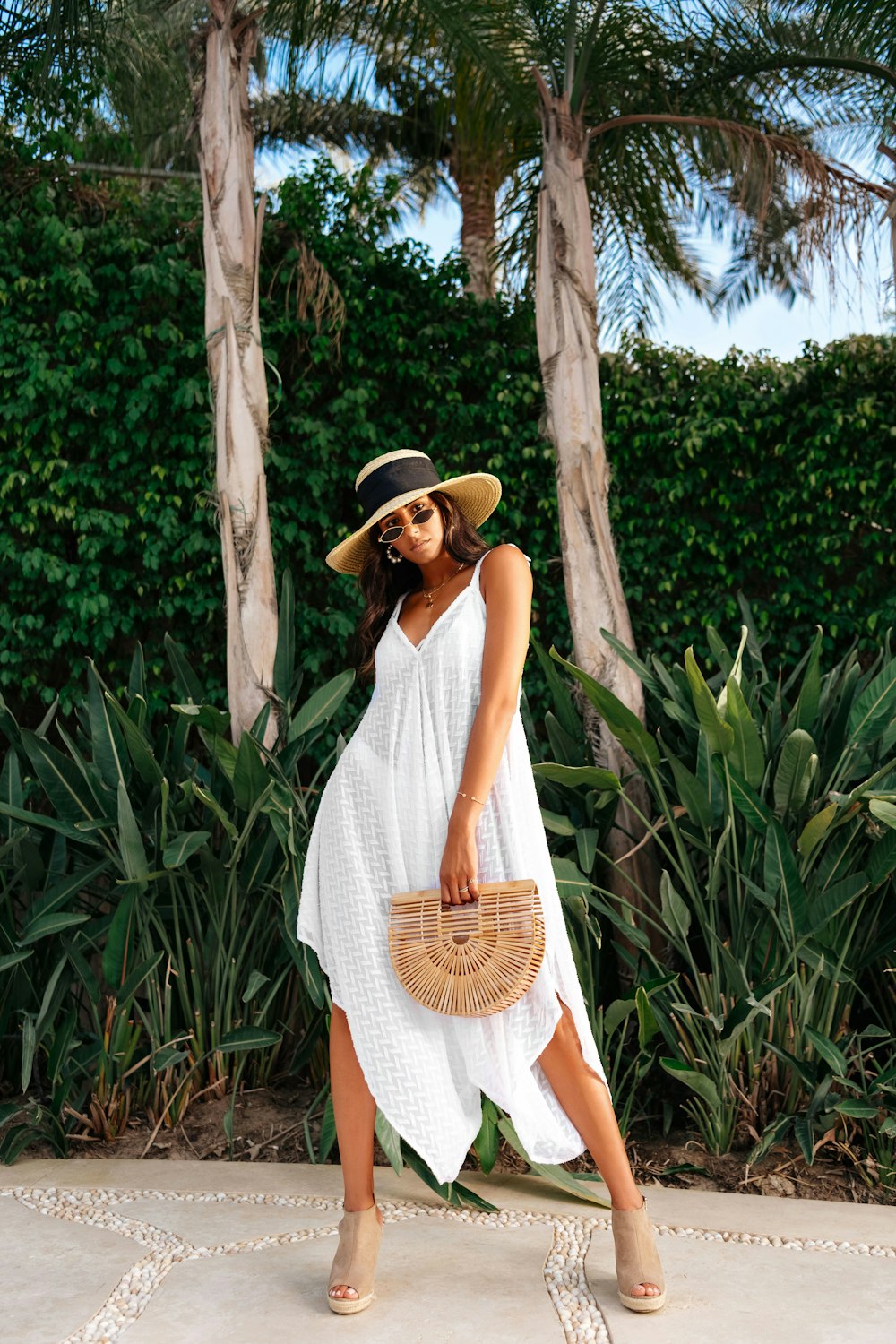 woman in white sleeveless dress wearing brown straw hat standing near green trees during daytime