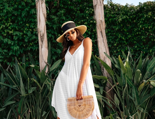 woman in white sleeveless dress wearing brown straw hat standing near green trees during daytime