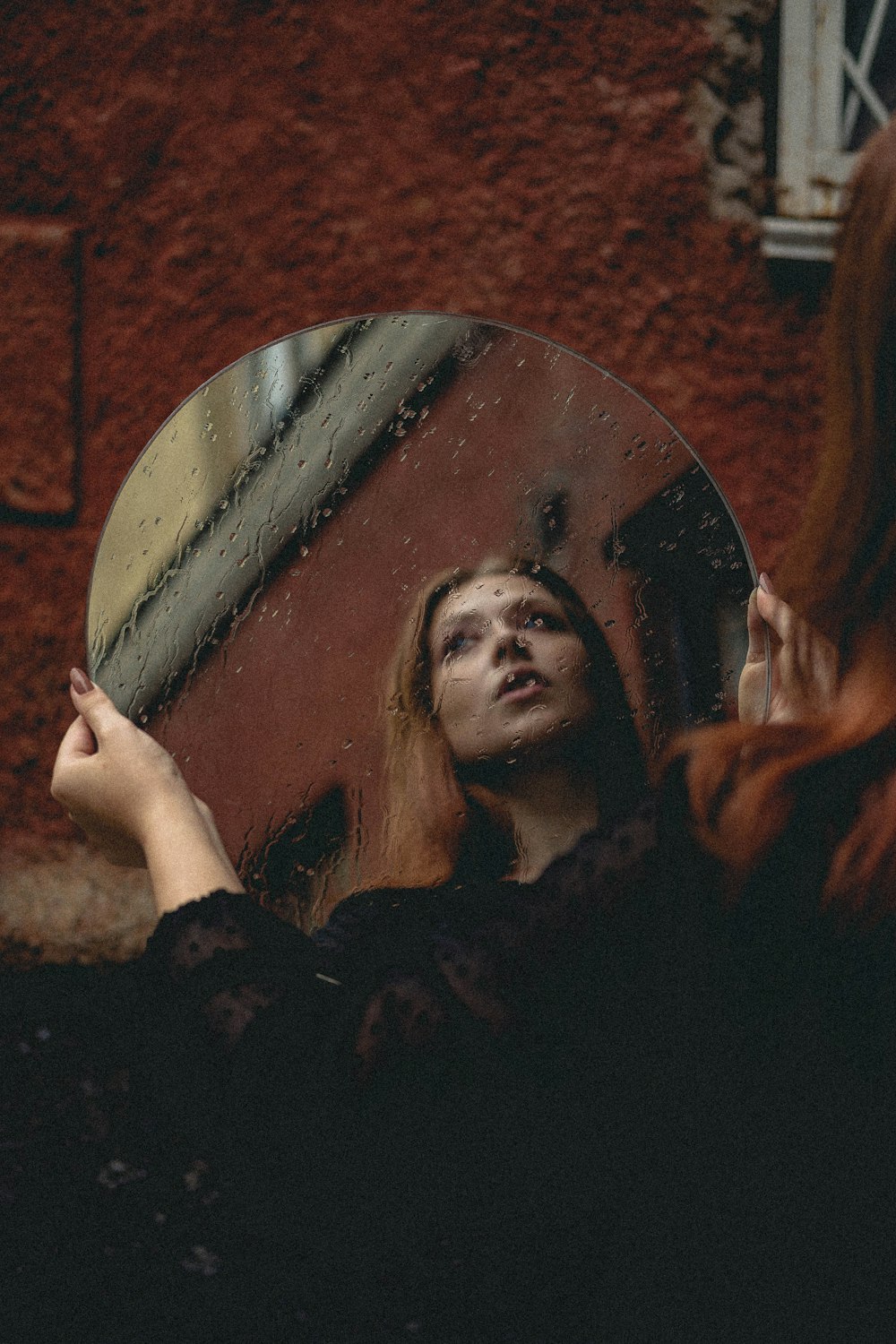 woman holding round mirror with brown wooden frame