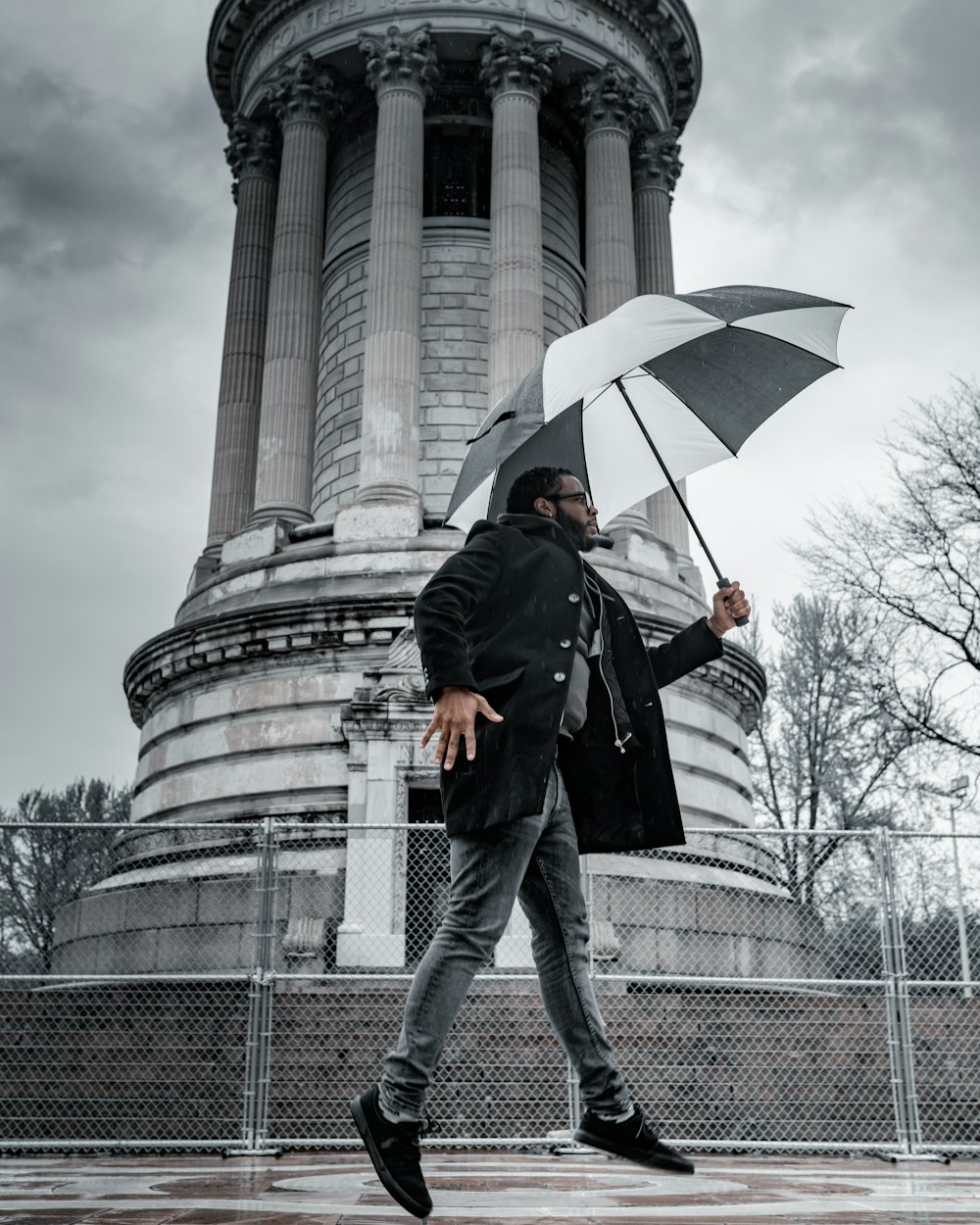 man in black jacket and black pants holding umbrella standing near gray concrete building during daytime