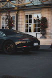 A sleek black sports car parked outside an opulent hotel entrance lit by golden lights.