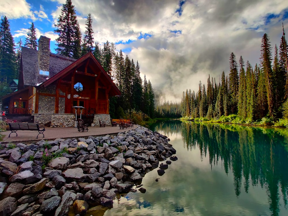 Braunes Holzhaus in der Nähe von grünen Bäumen und Fluss unter weißen Wolken und blauem Himmel während des Tages