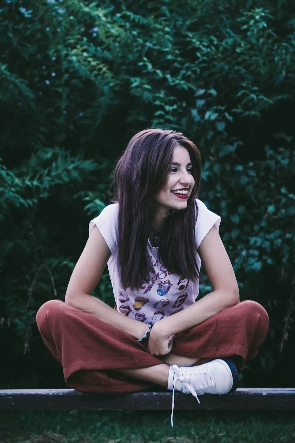 woman in white t-shirt and red pants sitting on green grass during daytime