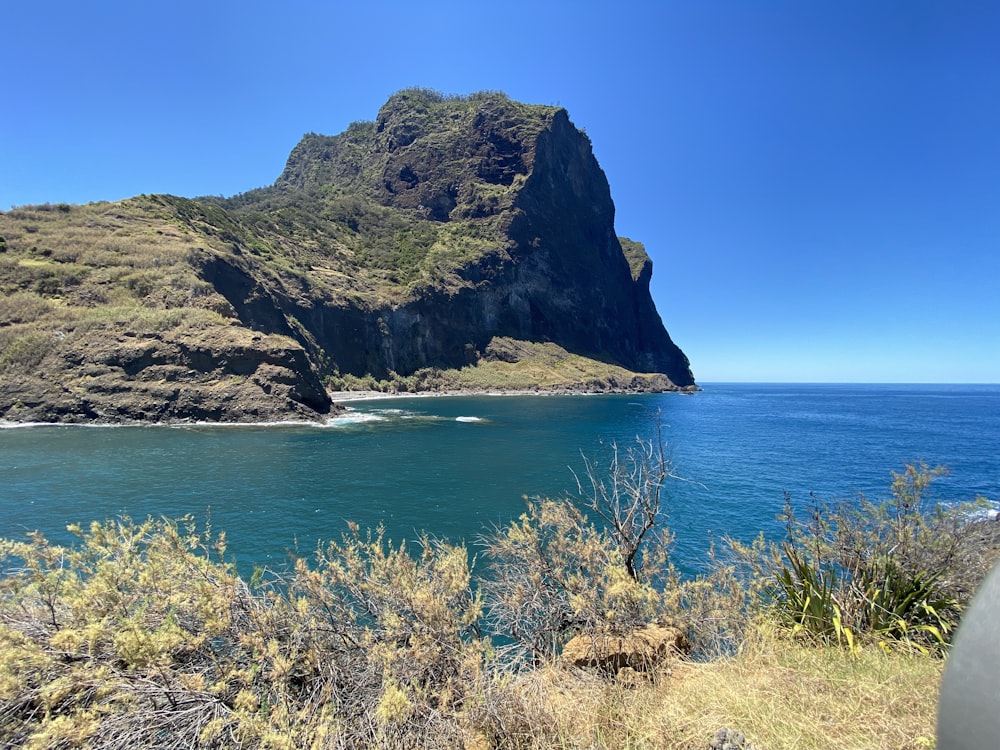 formazione rocciosa verde e marrone accanto al mare blu sotto il cielo blu durante il giorno