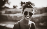 Woman wearing sleek cat-eye glasses smiling outdoors in soft sunlight.