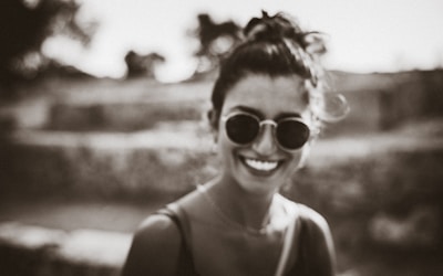 Woman wearing sleek cat-eye glasses smiling outdoors in soft sunlight.