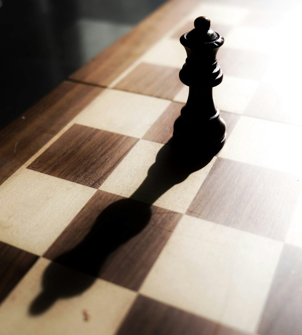 Pezzo degli scacchi nero su tavolo a scacchi marrone e bianco