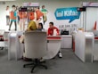A customer service area features a desk with two employees, one wearing a red uniform and the other assisting a customer. The setting includes a colorful backdrop with life-sized cutouts of young people and the word 'Loop' in large letters. The counter displays digital numbers, and promotional materials are placed on the desk.