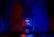 A microphone with a prominent brand logo and volume control knob, illuminated by dramatic red and blue lighting, creating a visually striking contrast.