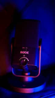 A RØDE microphone is centrally positioned, with prominent controls and branding visible. The microphone is illuminated by blue and red lighting, creating a striking contrast and highlighting its modern design.