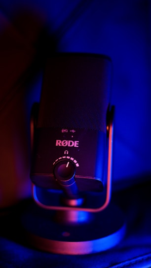 A RØDE microphone is centrally positioned, with prominent controls and branding visible. The microphone is illuminated by blue and red lighting, creating a striking contrast and highlighting its modern design.
