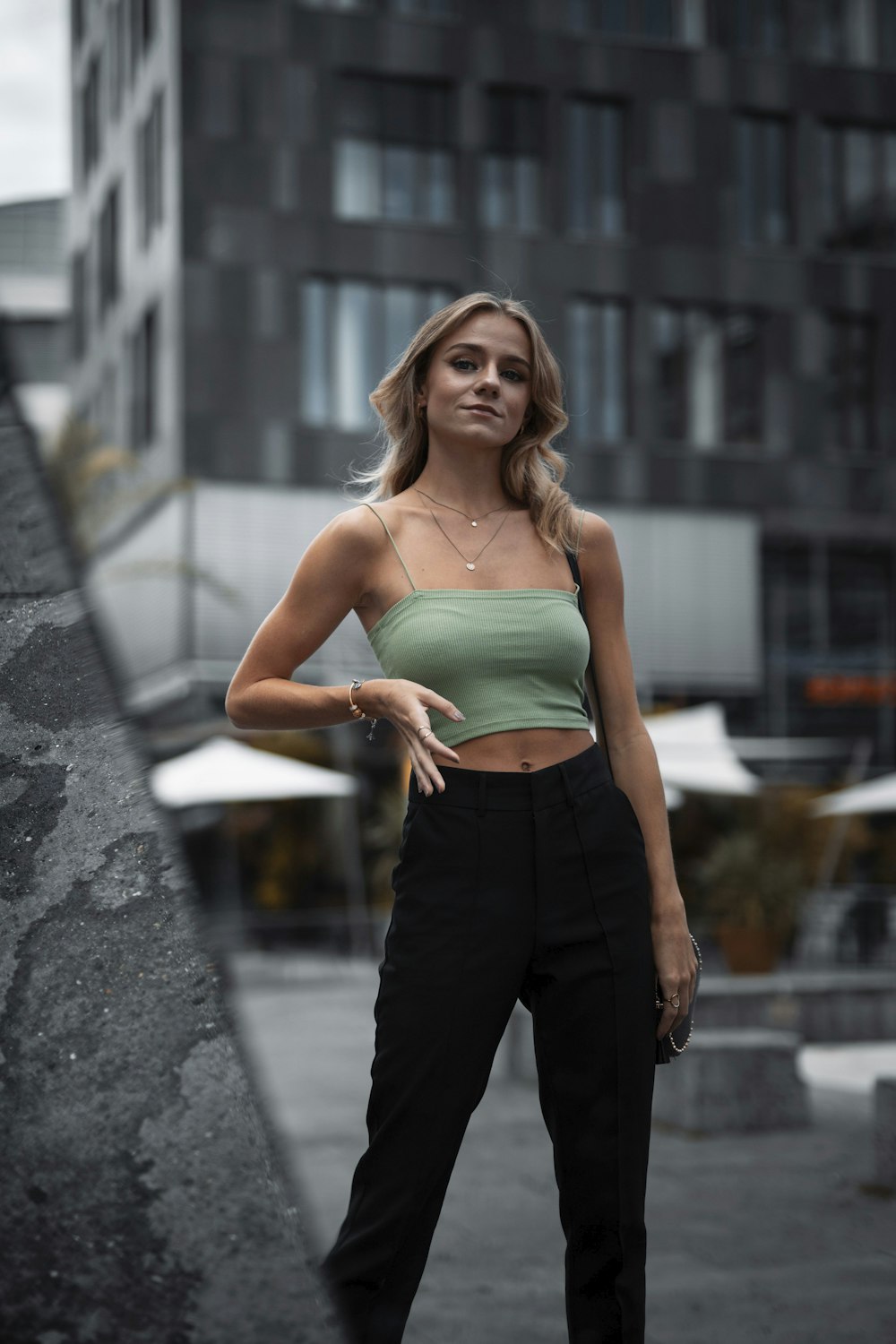 woman in teal tank top and black pants standing on gray concrete pavement during daytime