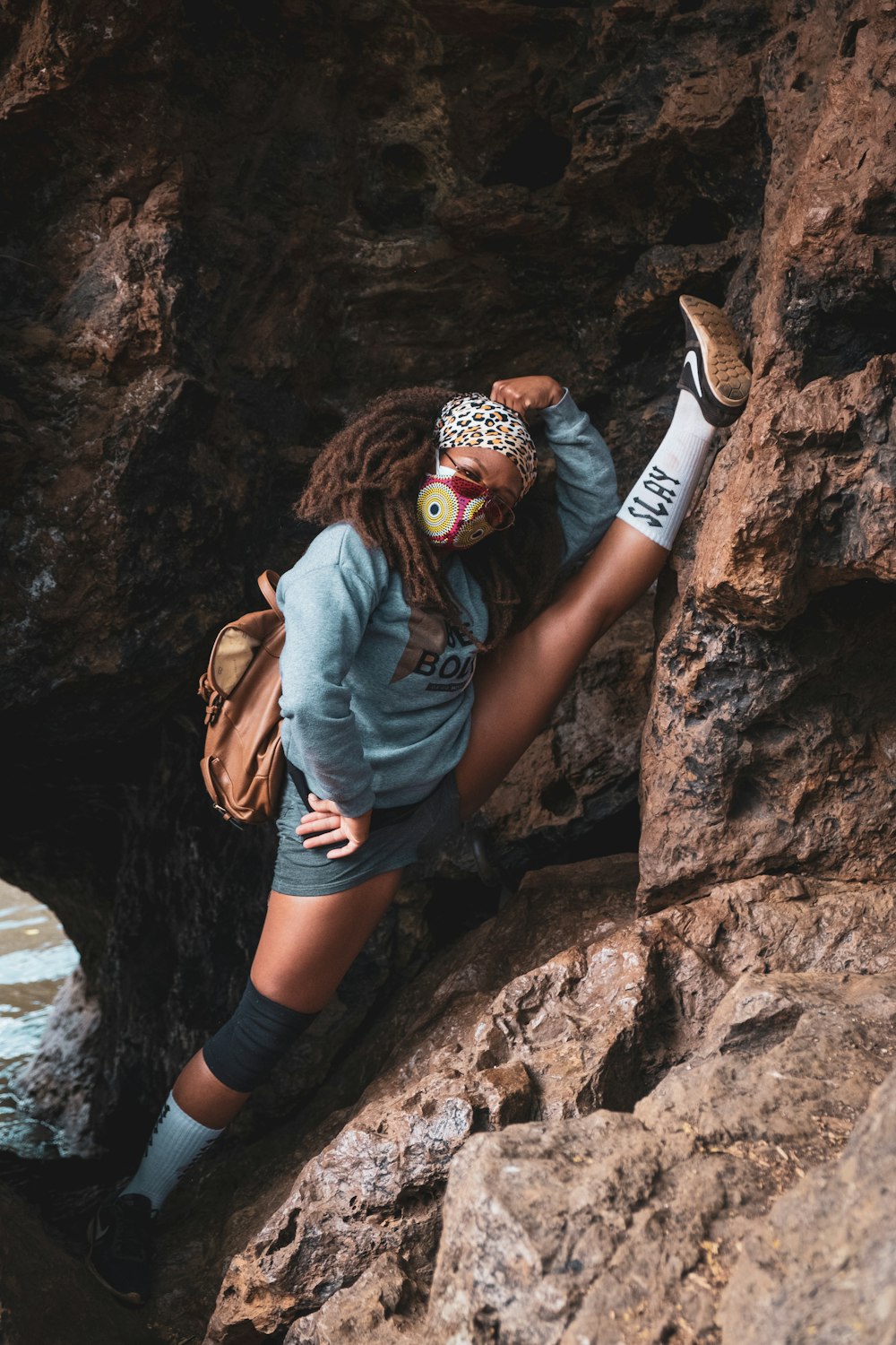 man in blue denim jacket and black shorts with brown backpack climbing on brown rock