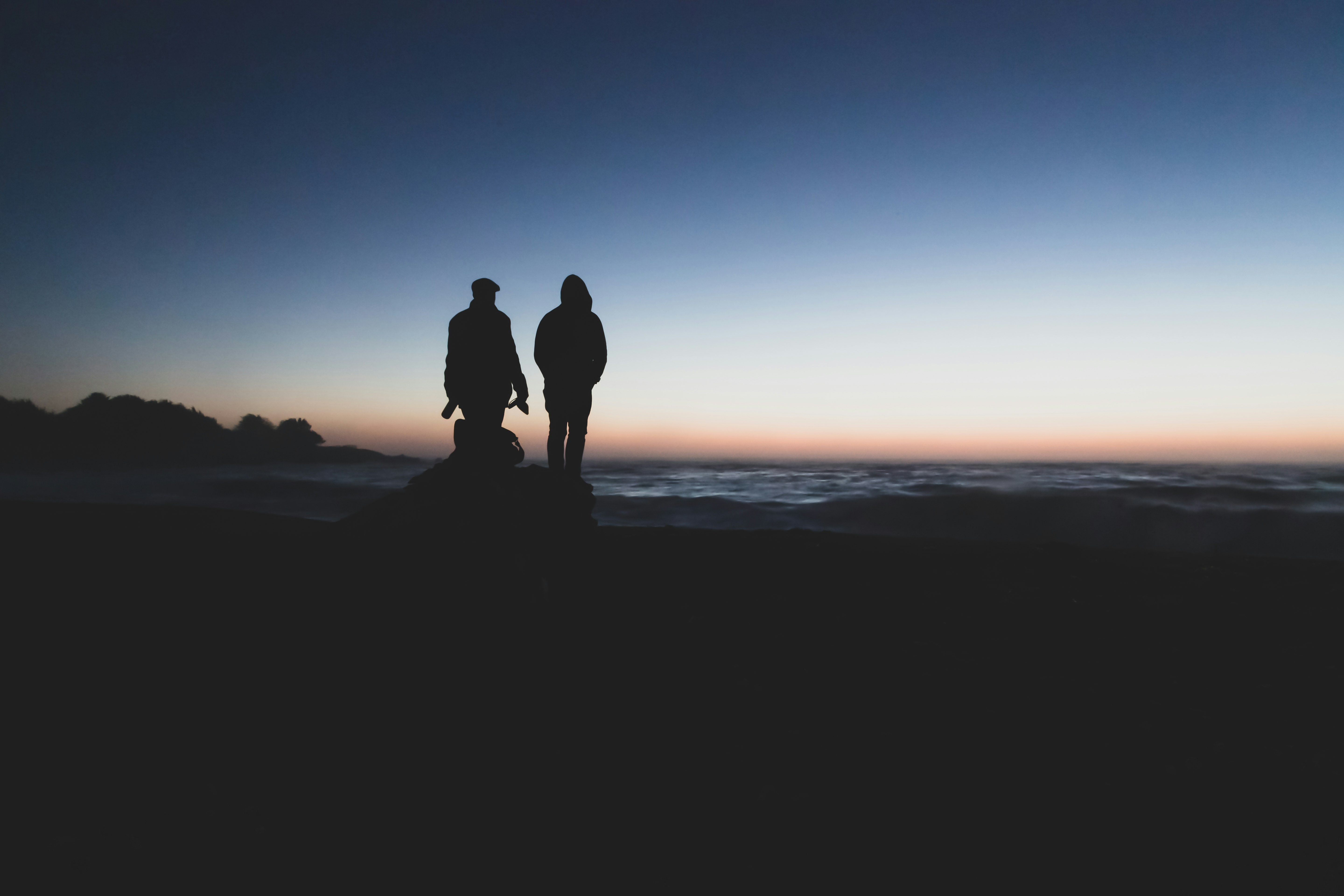 silhouette of 2 person standing on seashore during sunset