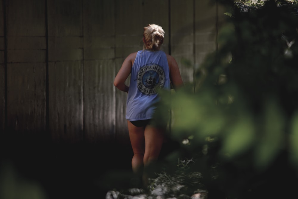 man in blue crew neck t-shirt and black shorts standing beside brown wooden wall during