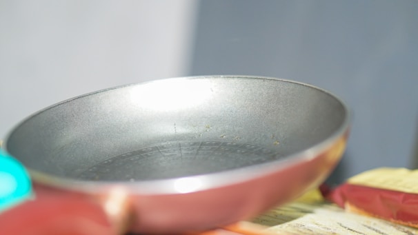 Close-up of a stainless steel frying pan with a wooden handle, sitting on a modern stovetop.