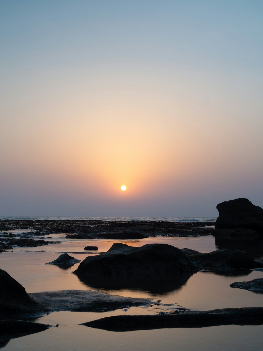 silhouette of rocks on sea shore during sunset