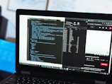 A laptop displaying a dual-screen setup with coding scripts on one side and a YouTube video on the other. The scripts are in a code editor, while the YouTube side shows a video tutorial about using the Fetch API in JavaScript. There are multiple tabs open, and a file explorer is visible.