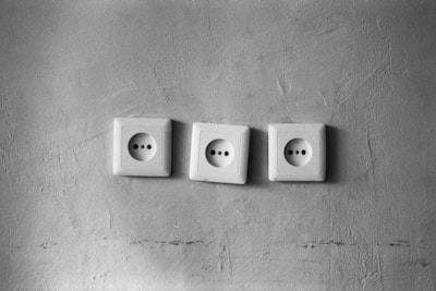 Three electrical outlets are arranged in a row against a textured wall. The wall appears slightly rough with visible marks and contours.
