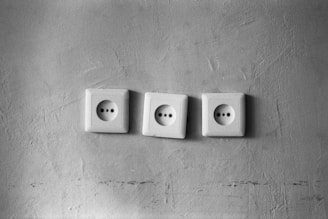 Three electrical outlets are arranged in a row against a textured wall. The wall appears slightly rough with visible marks and contours.