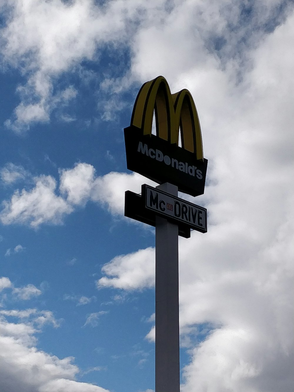 a mcdonald's and mcdonald drive sign under a cloudy blue sky