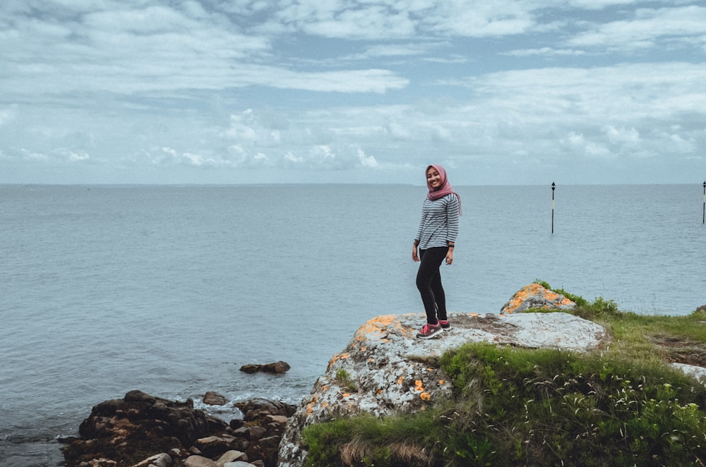 man in black and white striped long sleeve shirt standing on rock near body of water