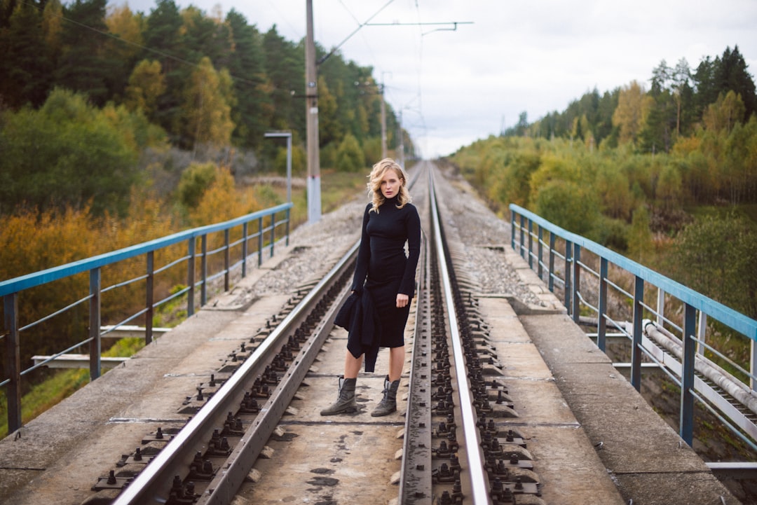 woman in black coat standing on train rail during daytime